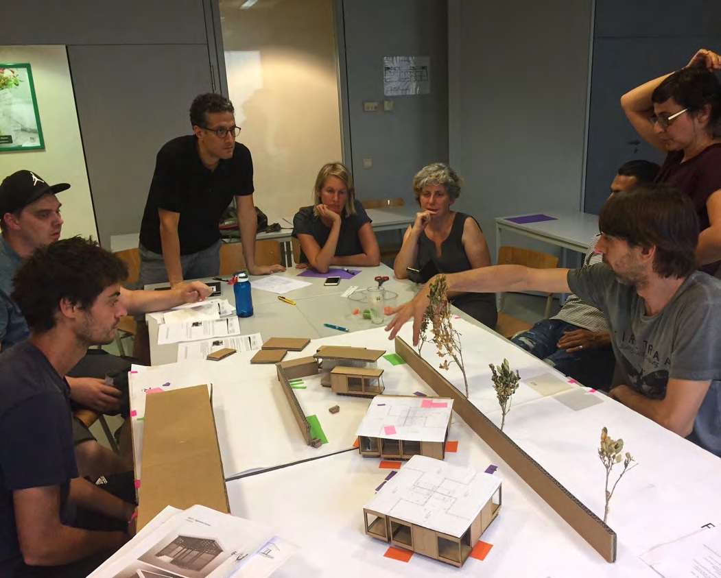 Solidary Mobile Housing participants discuss physical models around a table during a collective design session.
